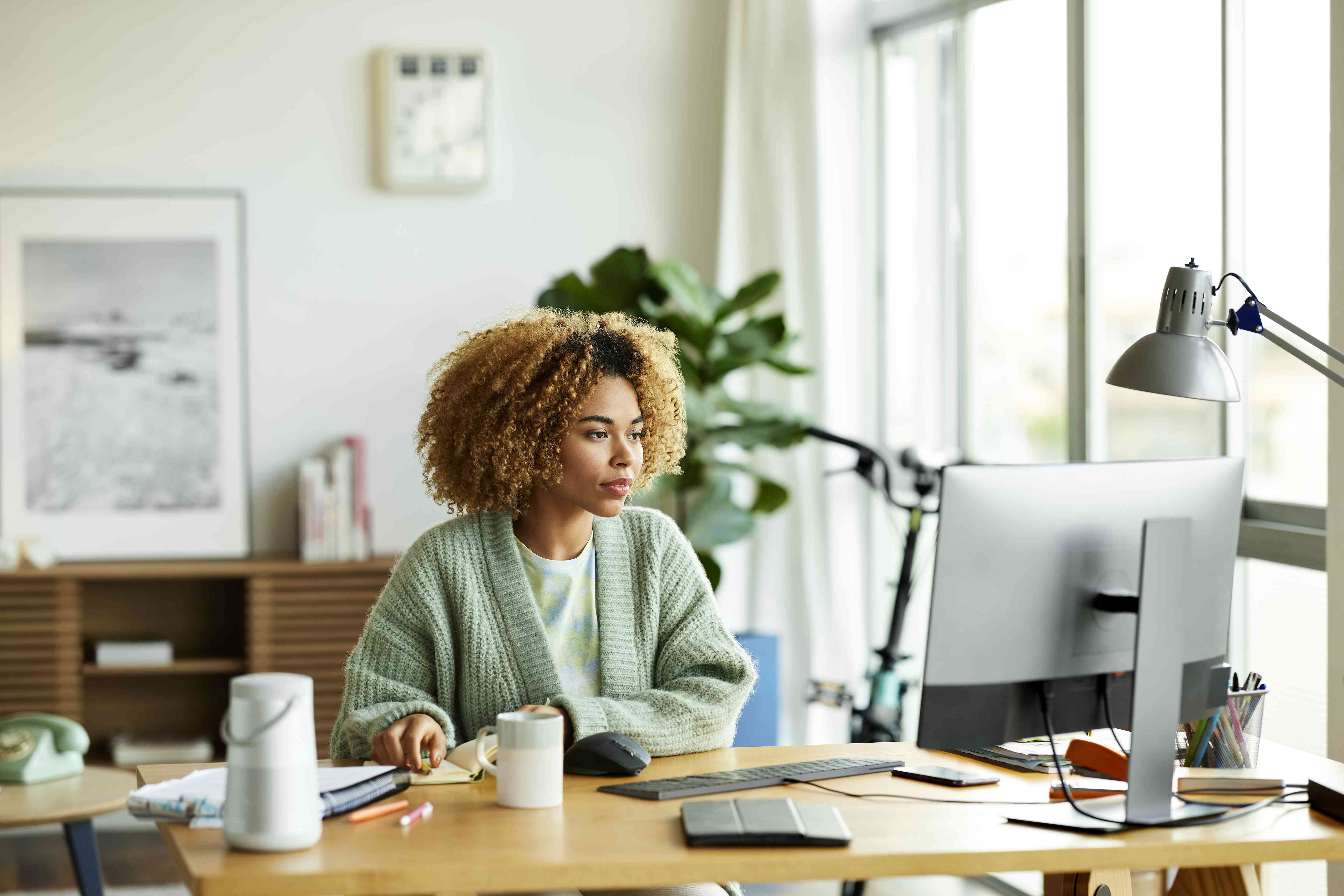 A woman sits at a desk in a home office working on a desktop computer 