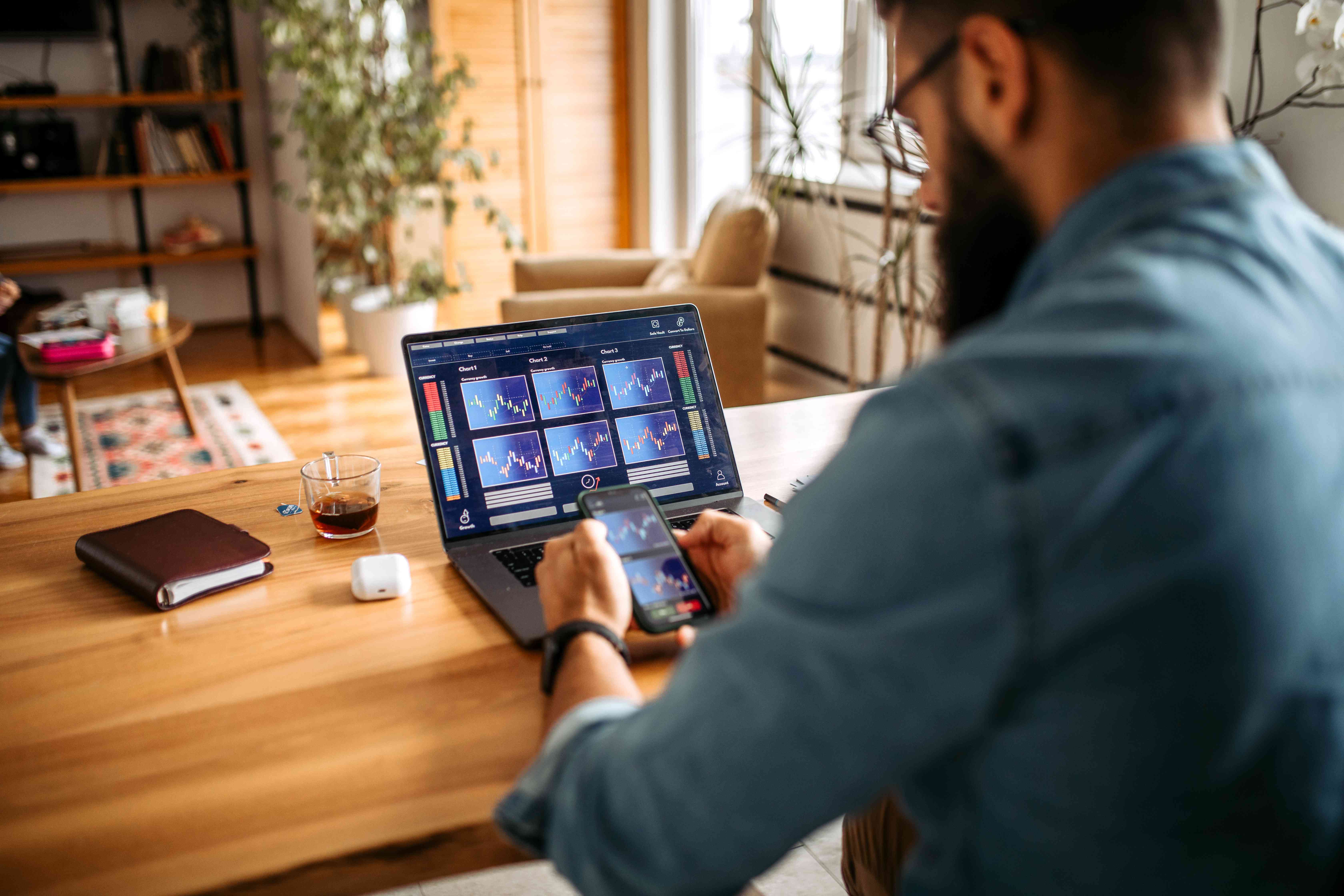 Crypto trader looking at charts on a laptop and phone.