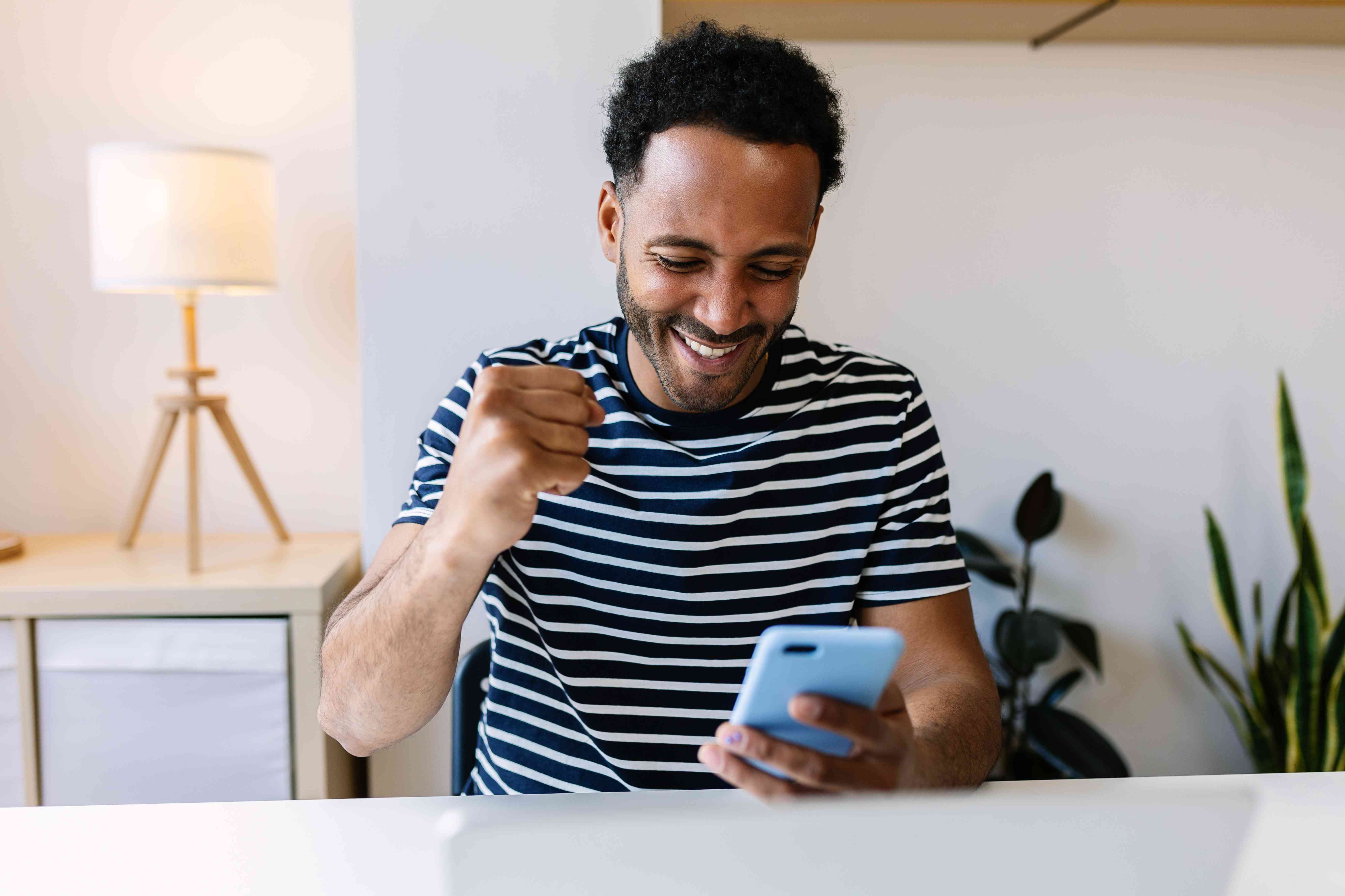 A young black man holding a phone and excitedly pumping his fist in the air in happiness.