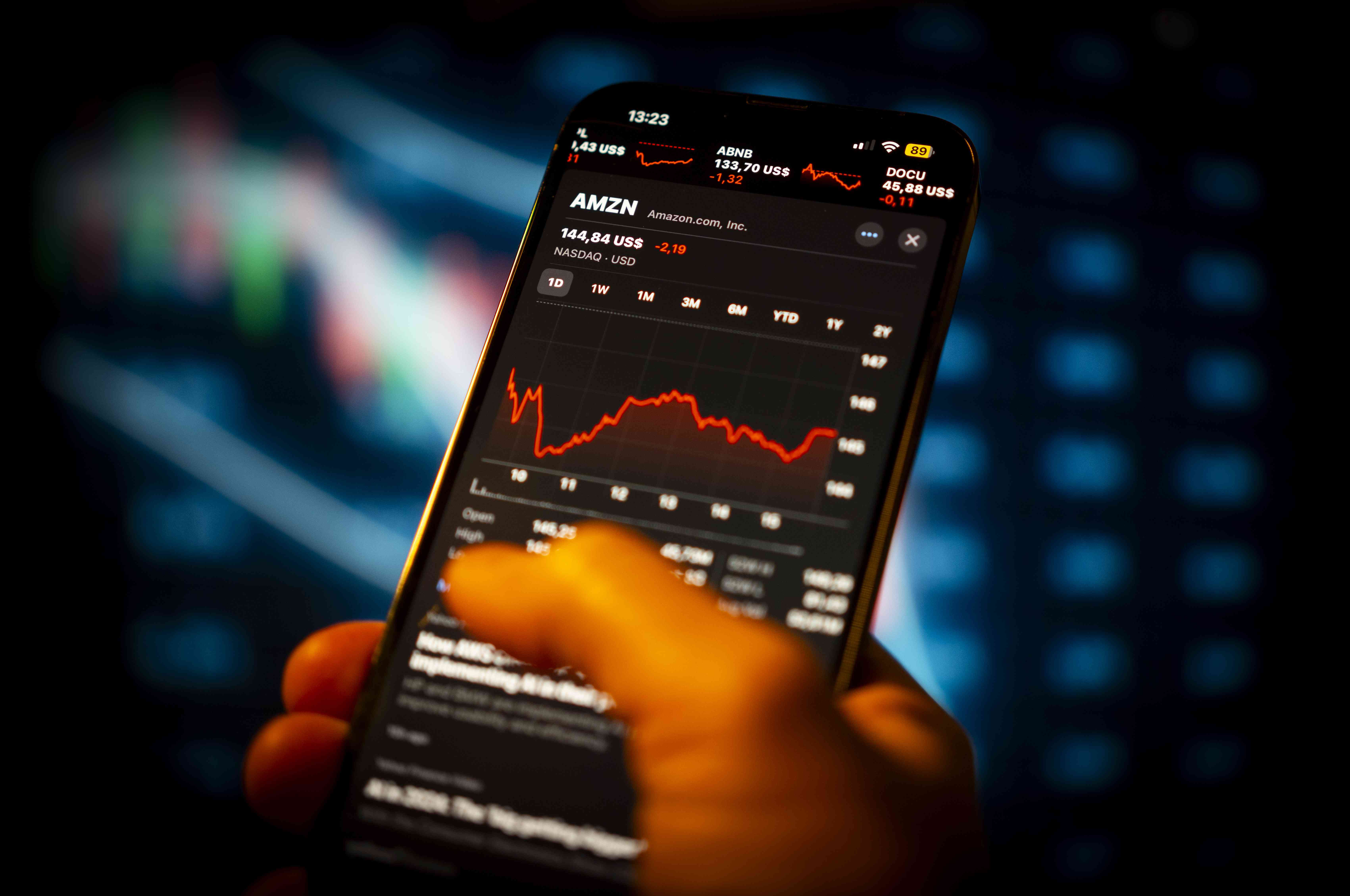 A person holds a phone displaying Amazon's stock price 