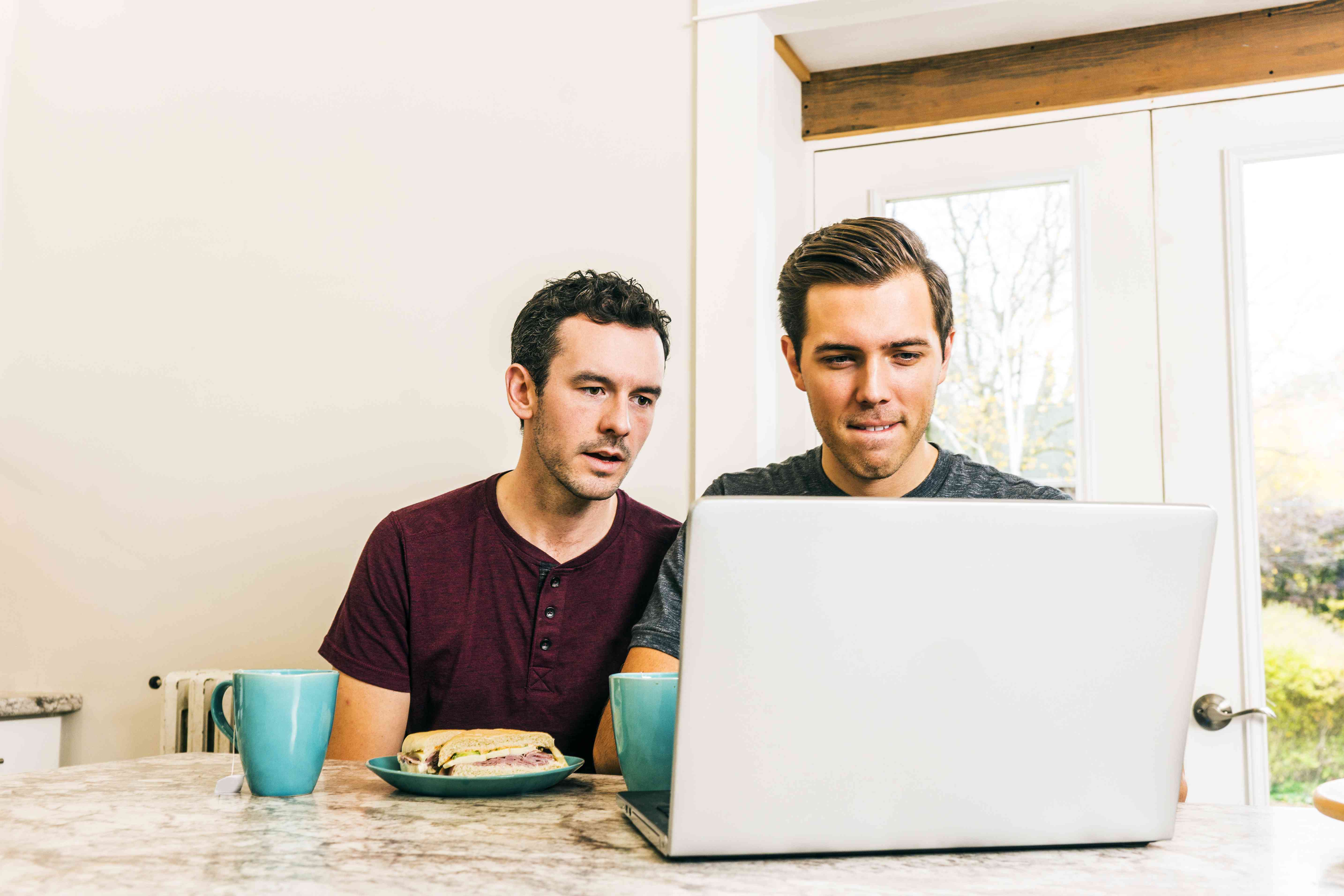 Two men review information on a laptop computer at home.