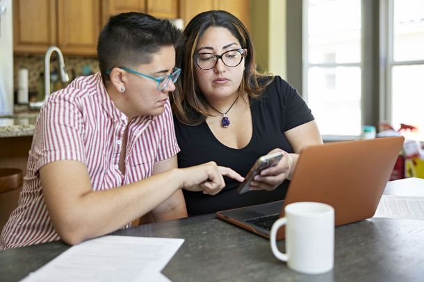 Two women reviewing paperwork with a smartphone and laptop at home